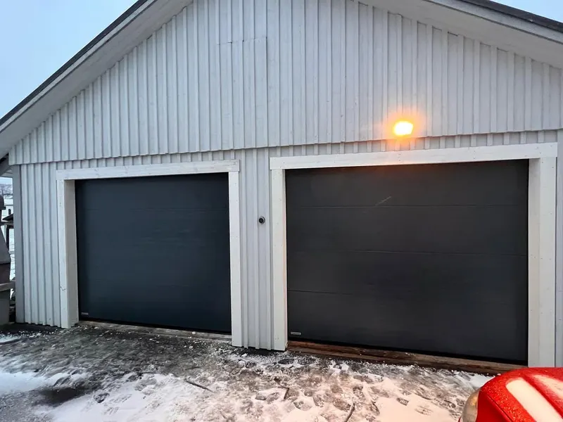Två svarta garageportar monterade på vit garagebyggnad i Sävsjö.