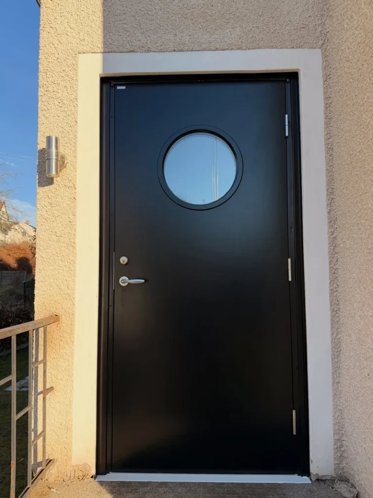 Svart Diplomat-ytterdörr med runt fönster monterad vid entré på hus i Jönköping.