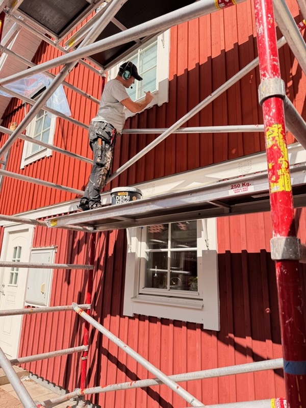 Målare från AF Byggservice målar vitt fönsterfoder för hand på en röd träfasad i Nässjö