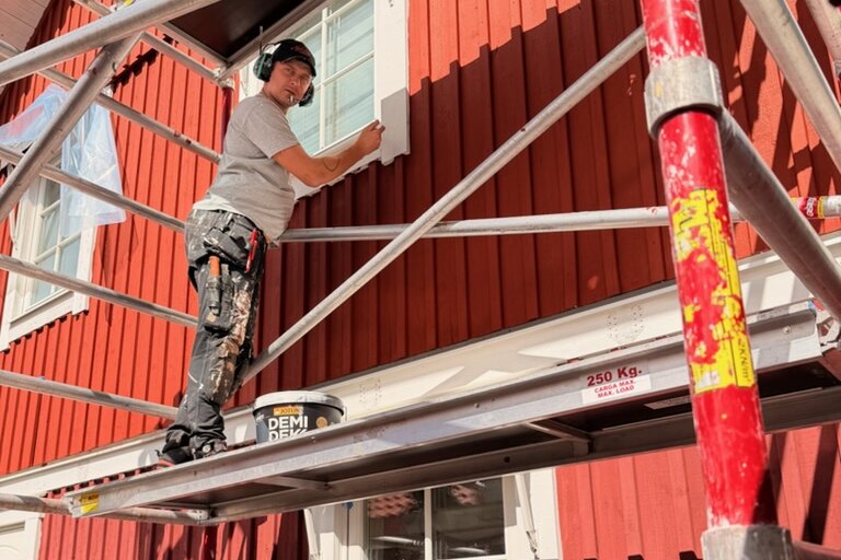 Målare från AF Byggservice målar fönsterfoder från ställning på en röd träfasad i Nässjö