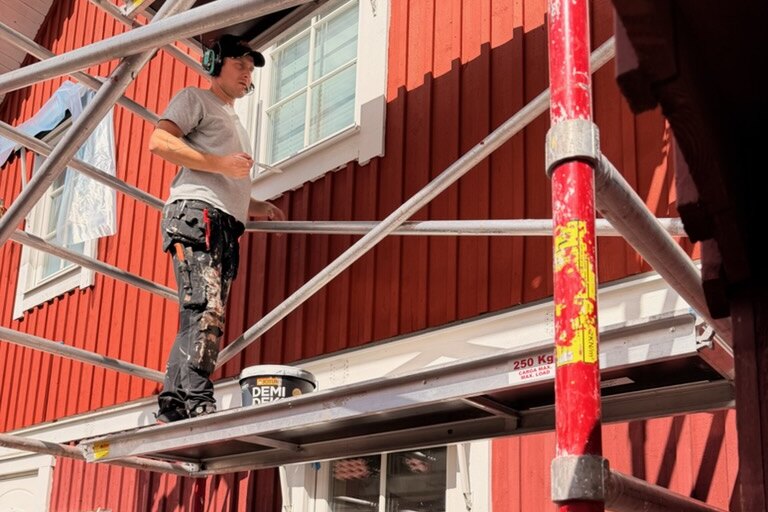 Ställning uppsatt längs en röd träfasad i Nässjö där AF Byggservice målar om huset