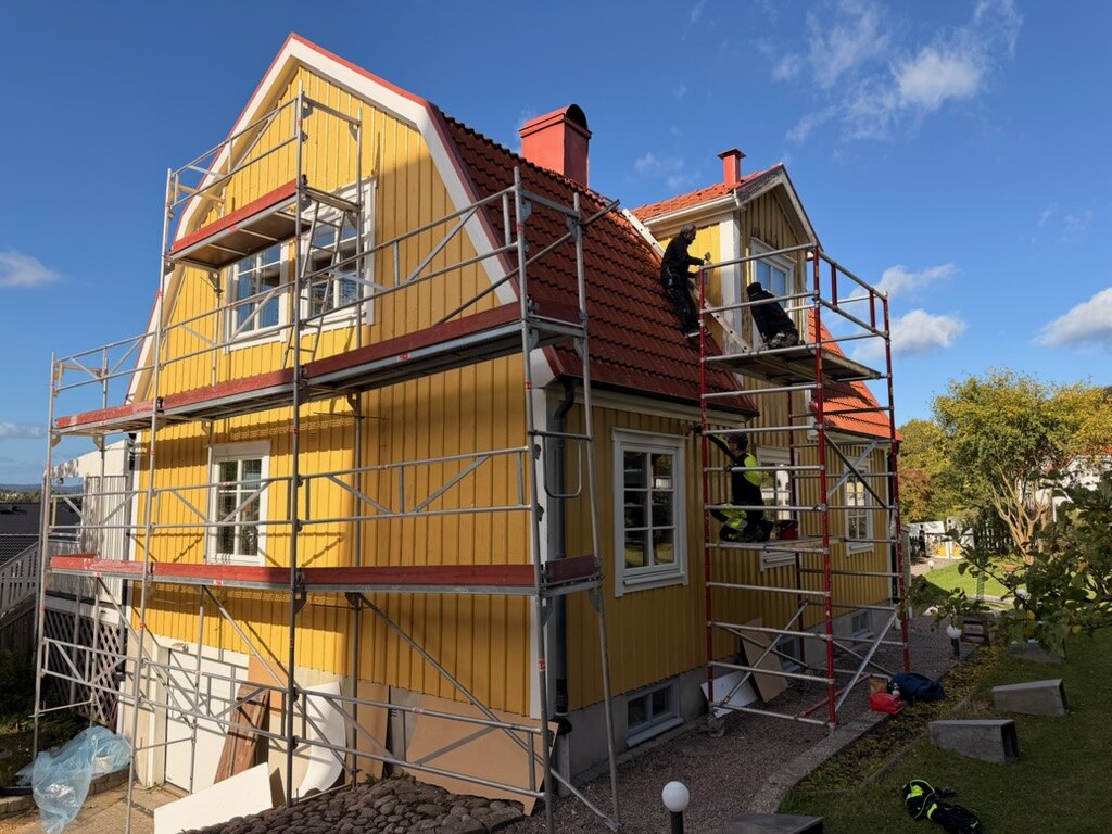 Ställning rest längs gavel och långsida på ett gult trähus under fasadmålning av AF Byggservice i Jönköpings län