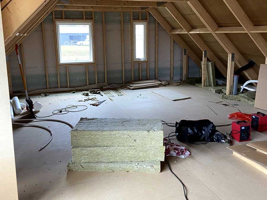 Kallvind i Eksjö med fackverkstakstolar, vindskydd på gavelväggen och paket med isolerskivor på golvet innan isoleringen läggs
