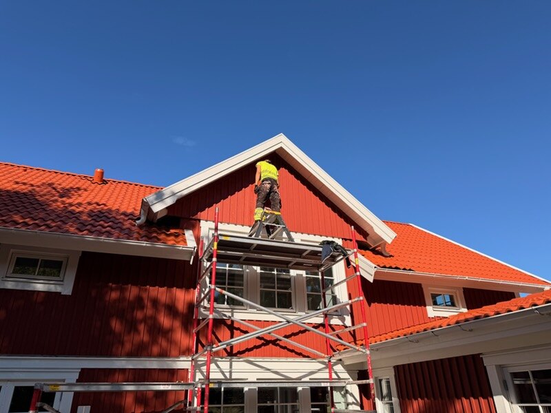 Målare från AF Byggservice på ställning vid gaveln på ett rött trähus i Jönköpings län
