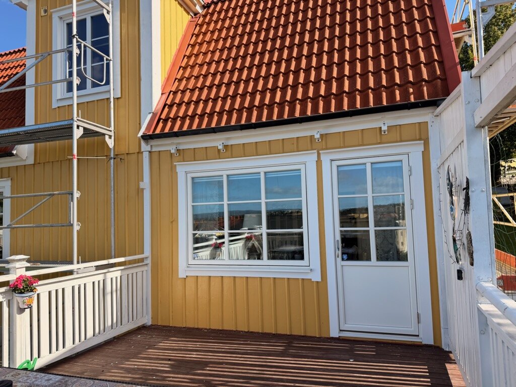 Nymålad gul träpanel med vita fönsterfoder och vit altandörr efter fasadmålning av AF Byggservice i Jönköpings län