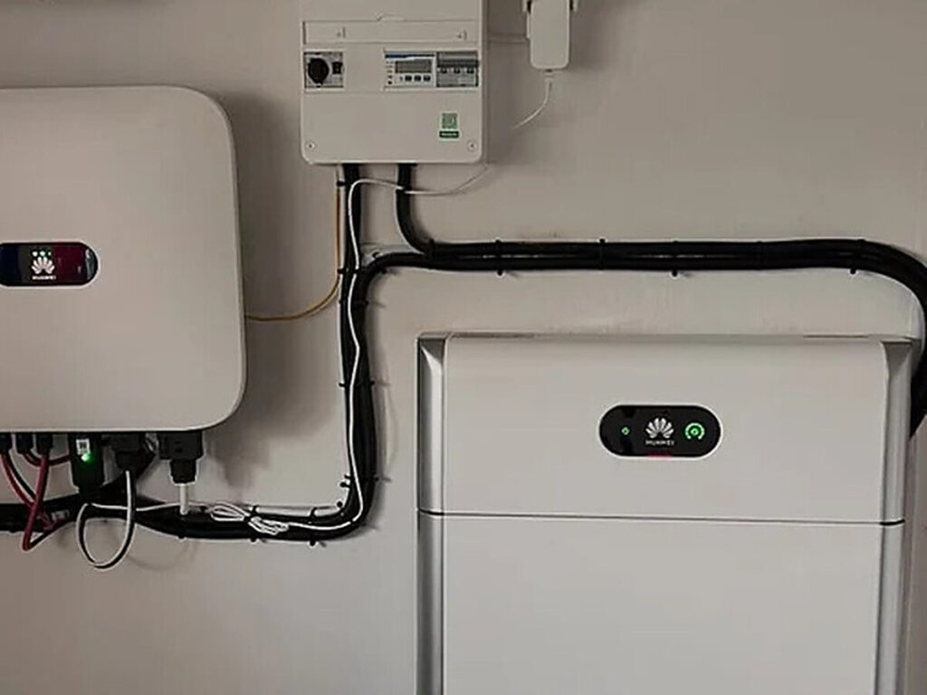 Liten elcentral med brytare, mätare och säkringar på väggen bredvid växelriktare och batteri i ett teknikrum i Vaggeryd, installerad av AF Byggservice