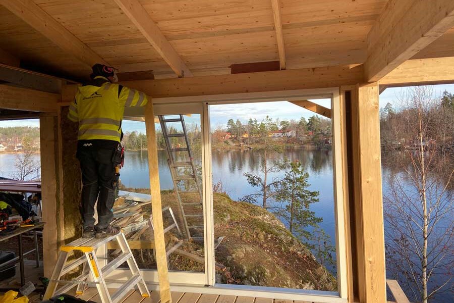 Inglasat uterum under byggnation på en altan i Nässjö, med stora glaspartier mot sjön och en snickare från AF Byggservice på stege vid takets infästning