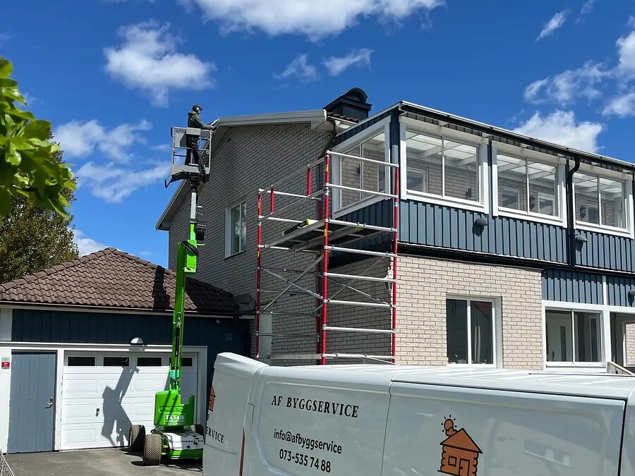 Snickare från AF Byggservice i skylift vid takfoten på en villa i Jönköpings län, med ställning och servicebil nedanför